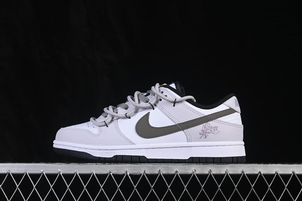 Side view of a white Nike SB Dunk Low sneaker with a dark gray Swoosh, black outsole, and floral heel graphic