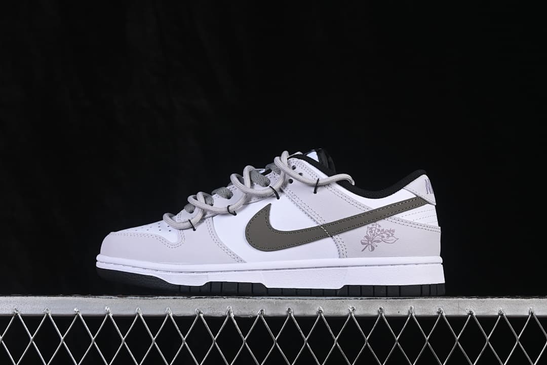 Side view of a white Nike SB Dunk Low sneaker with a dark gray Swoosh, black outsole, and floral heel graphic