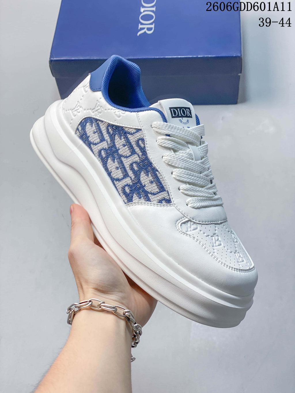 Angled view of the white sneaker with blue patterned side panels, blue collar accents, and a thick sole; image marking shows sizes 39–44.