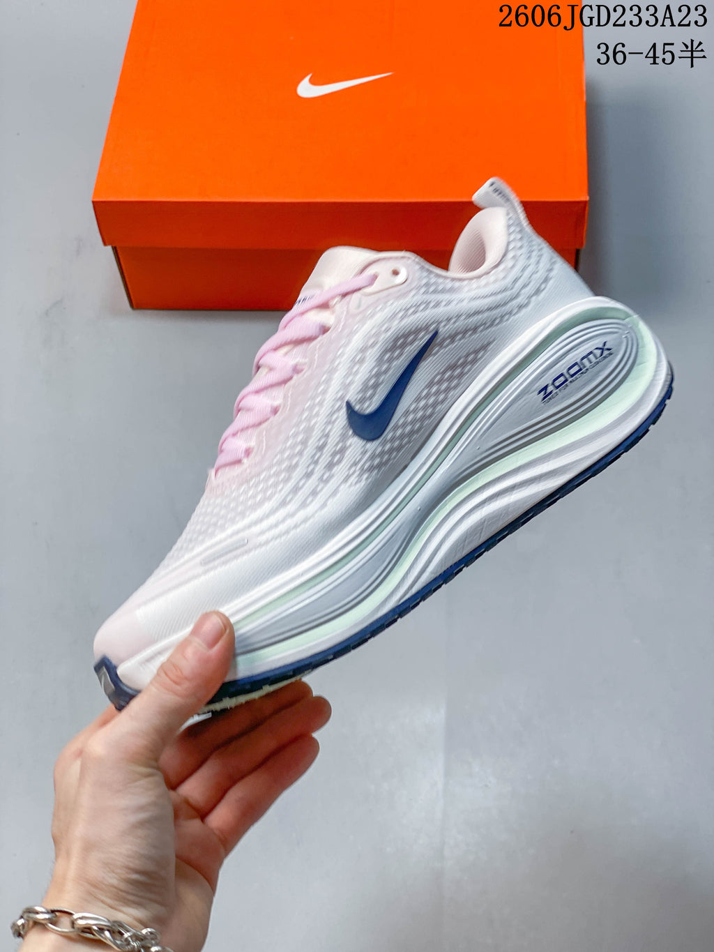Side view of the white Nike Vomero Plus shoe with blue Swoosh detail, pale pink accents, and sculpted midsole.