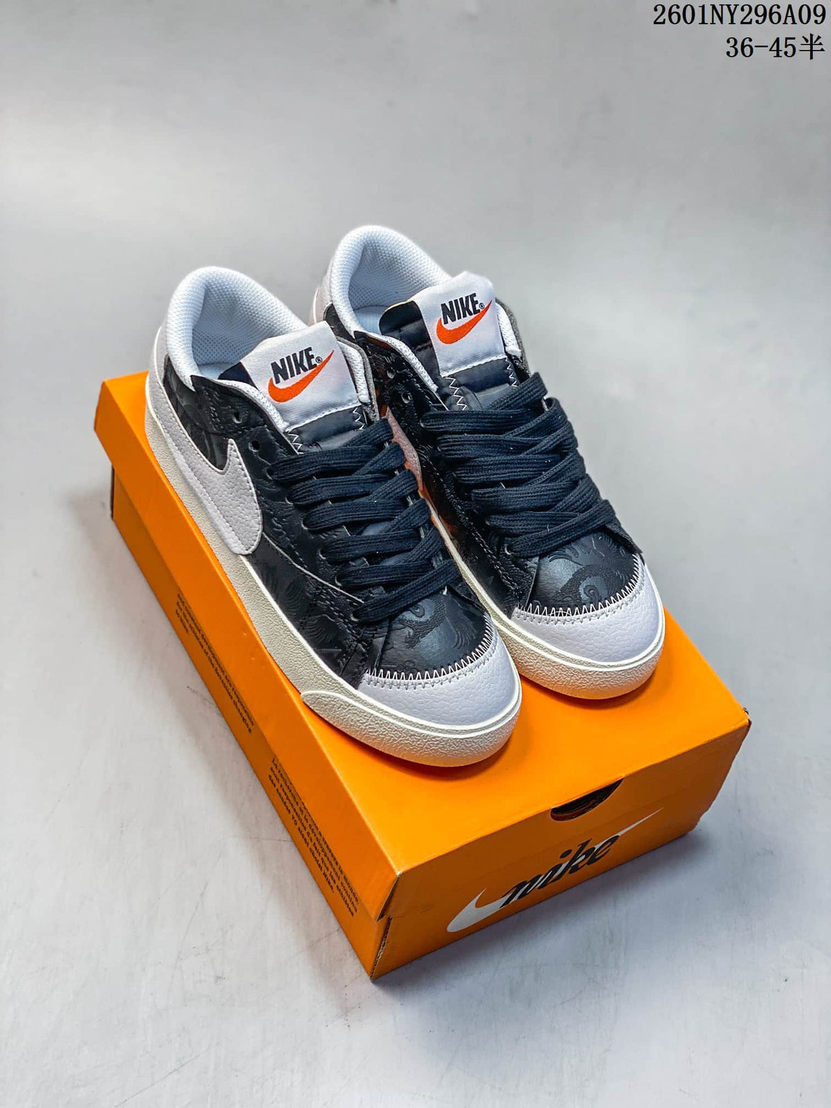 Pair of dark patterned Nike Blazer Low '77 Jumbo sneakers with white Swooshes and orange tongue accents.