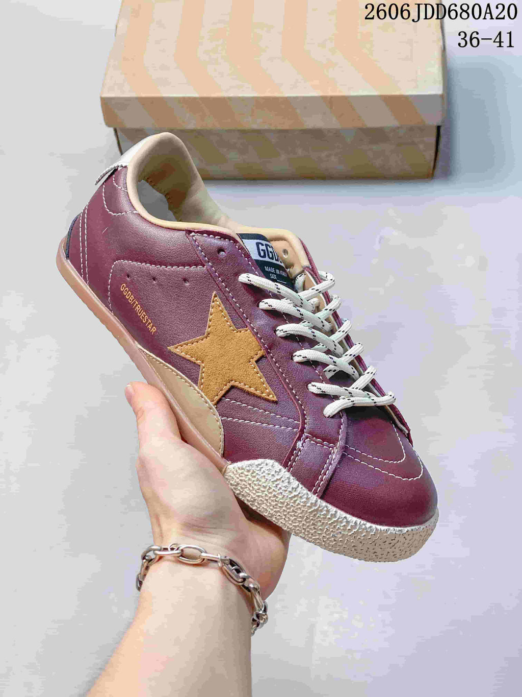 Close view of a burgundy sneaker with a tan star, white laces and textured off-white toe bumper