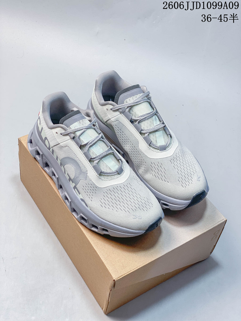 Pair of light gray On Cloudmonster Void low-top shoes on a box, with gray laces and an open-channel sole.