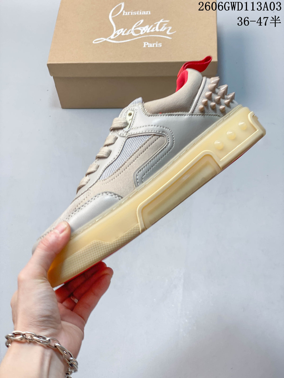 Side view of a sneaker with beige and light gray panels, heel studs, and a thick translucent-look sole