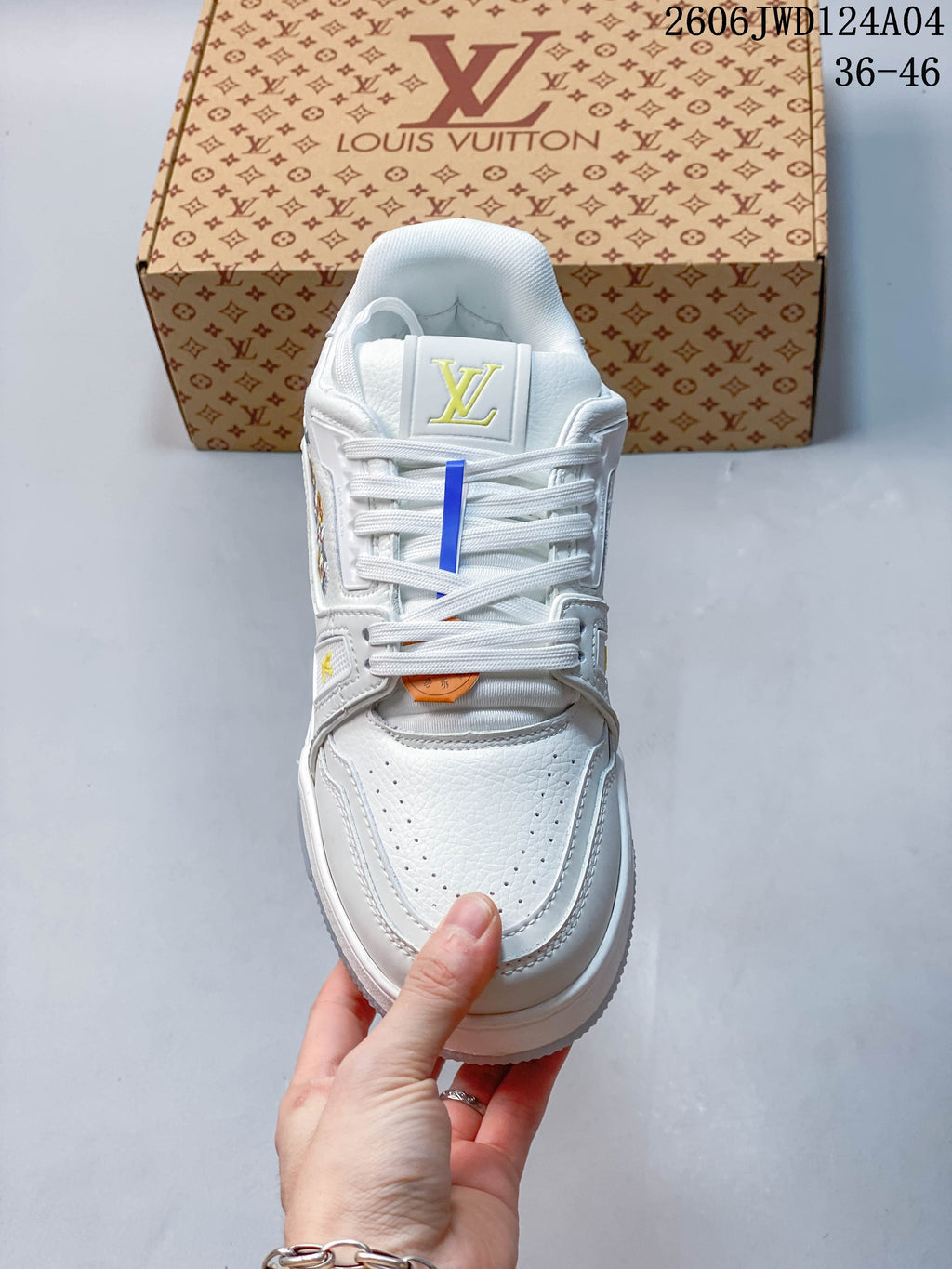 Front view of a white lace-up sneaker with a perforated toe, tongue emblem, and yellow accents.