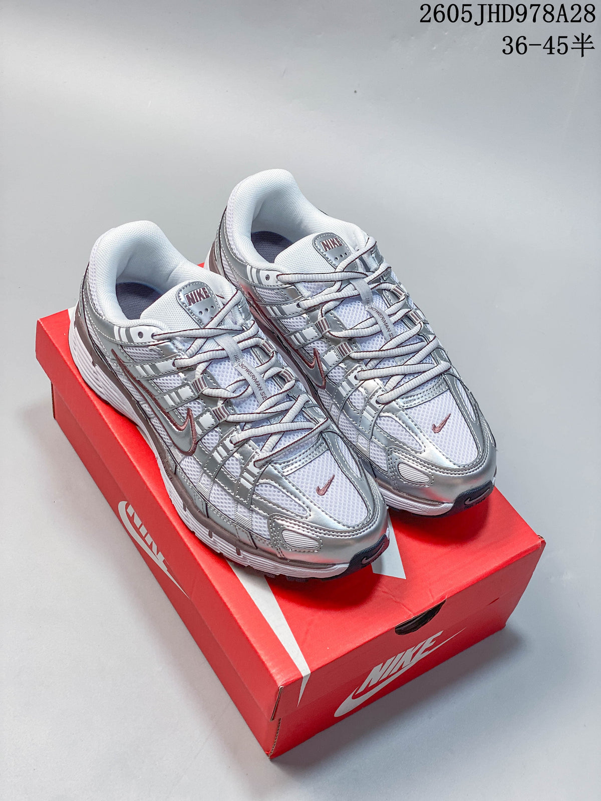 Pair of silver and white Nike Initiator running shoes displayed on a red box