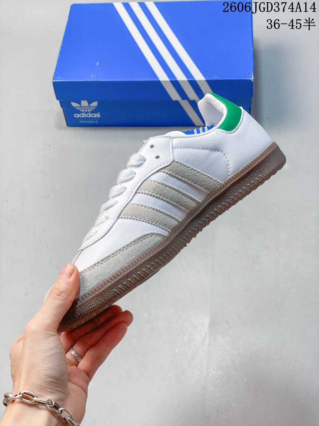 Side profile of a white low-top sneaker with gray overlays, three stripes, green heel accent, and gum-colored sole.