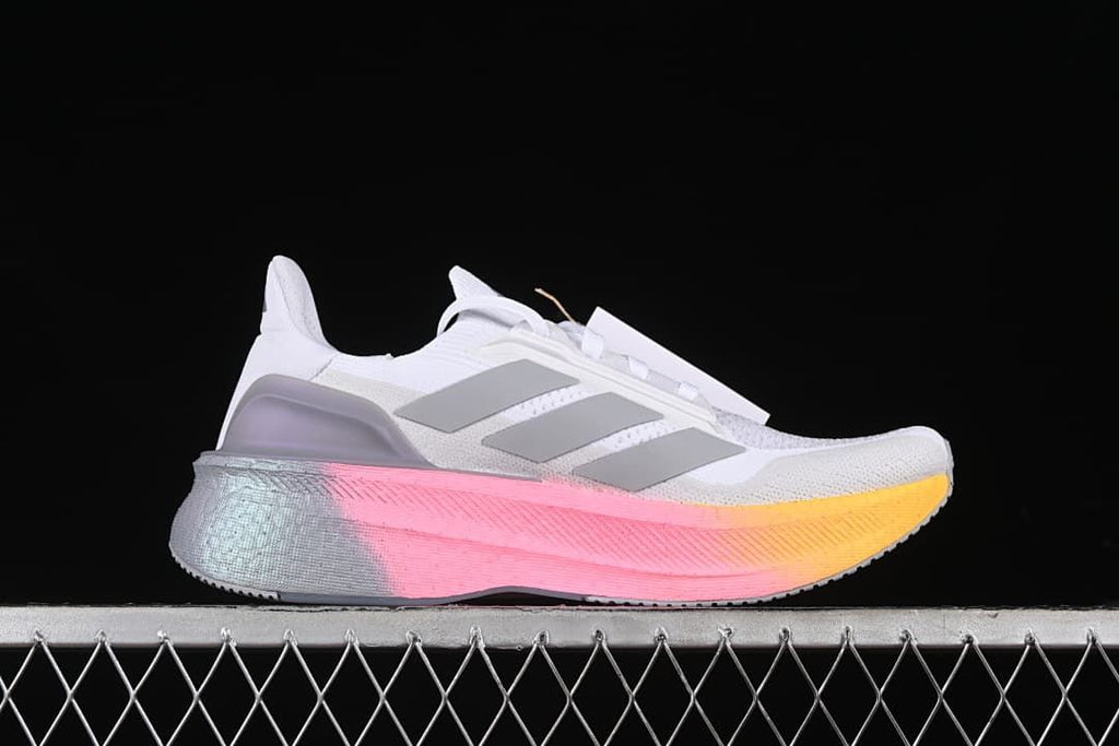 Side profile showing white upper, grey stripes and pink-to-yellow midsole