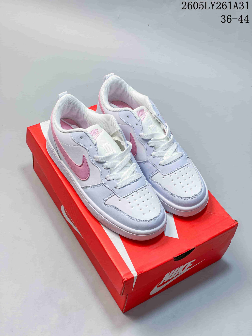 White and pink NikeCourt Borough Low Essential+ sneakers displayed on a red shoebox