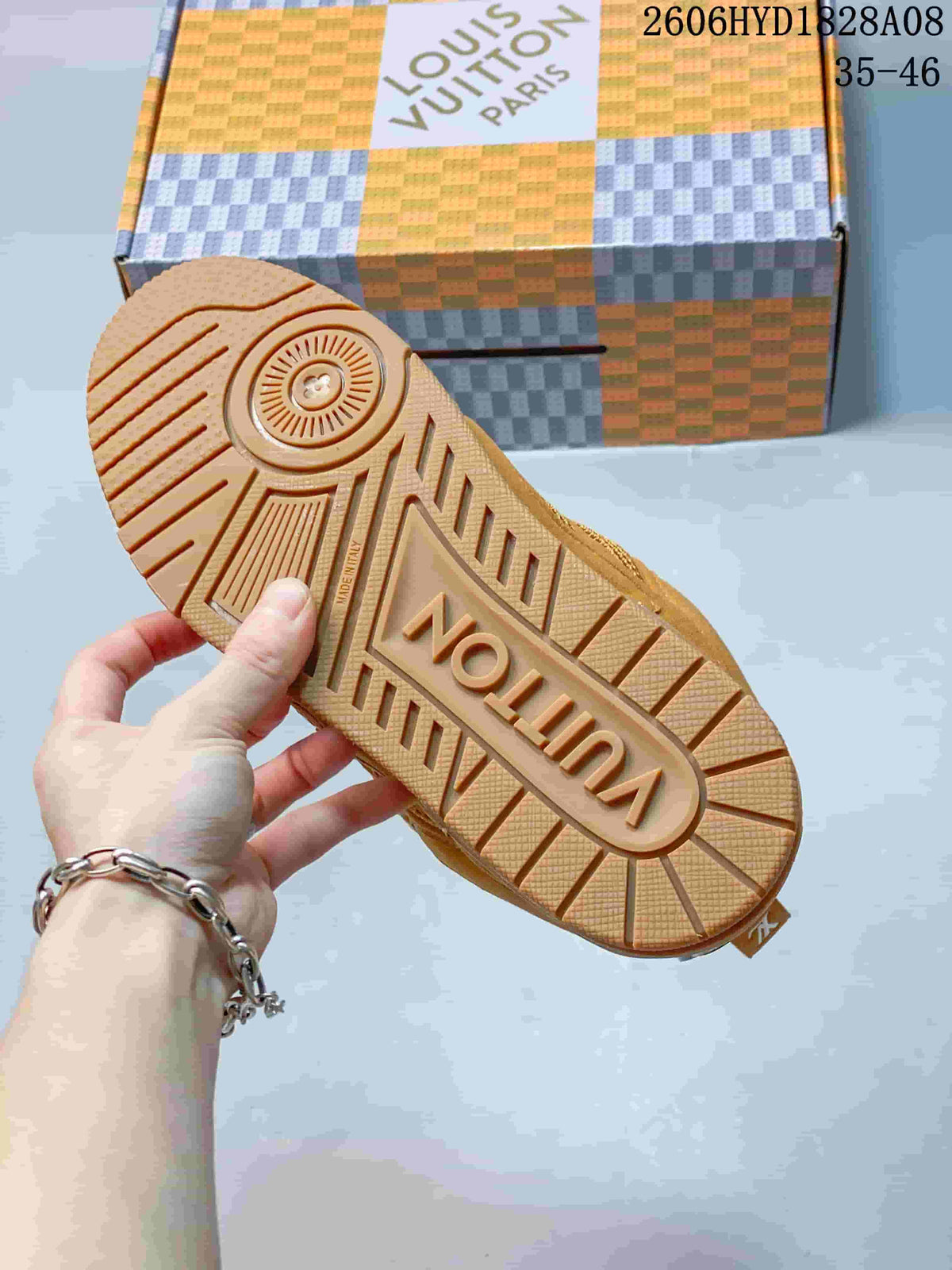 Outsole view of a brown sneaker with a patterned tread and branded box in the background
