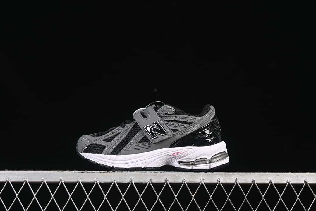 Black and gray kids’ sneaker with hook-and-loop straps and a white midsole, shown against a dark background.