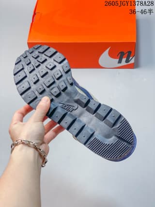 Underside view of the sneaker showing its dark tread pattern; orange box and sample-size marking in the background.