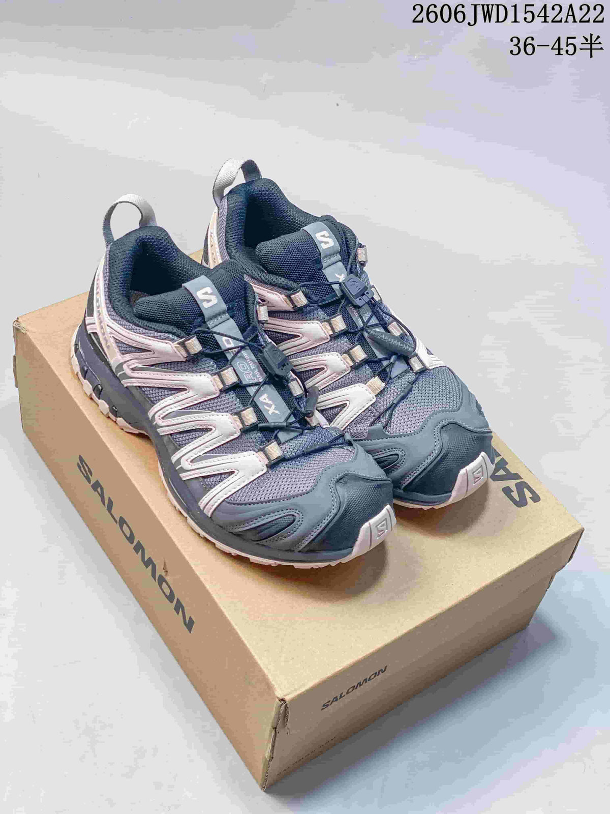 Pair of navy, gray, and pale pink Salomon XA Pro trail-style sneakers on a branded box