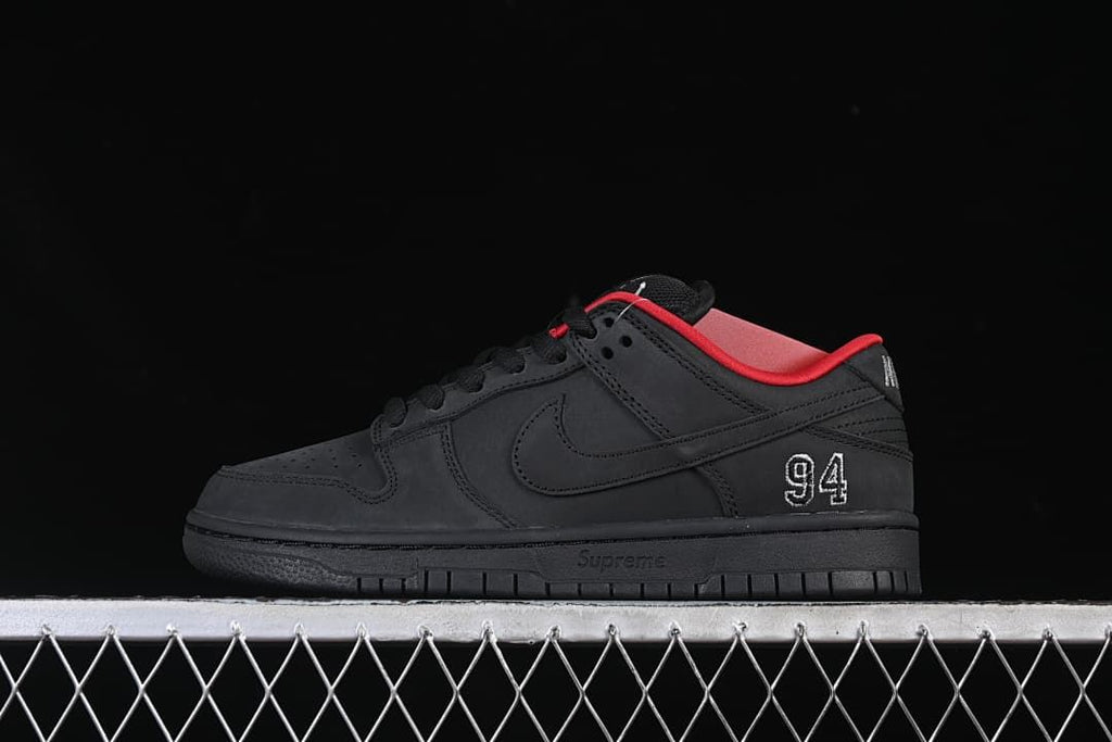 Side view of a black Nike SB Dunk Low with red collar lining and white 94 heel embroidery
