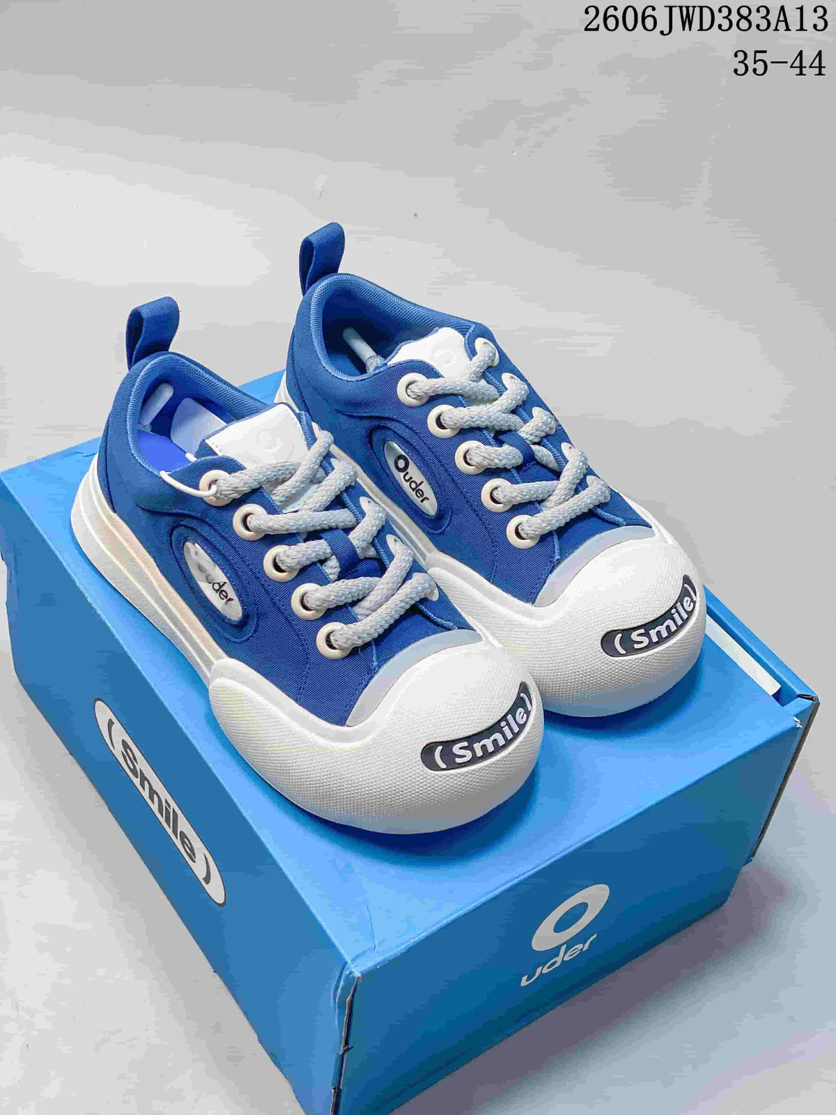 Blue Ocai 002 Smile low-top sneakers with white laces and oversized white toe bumpers on a blue box.