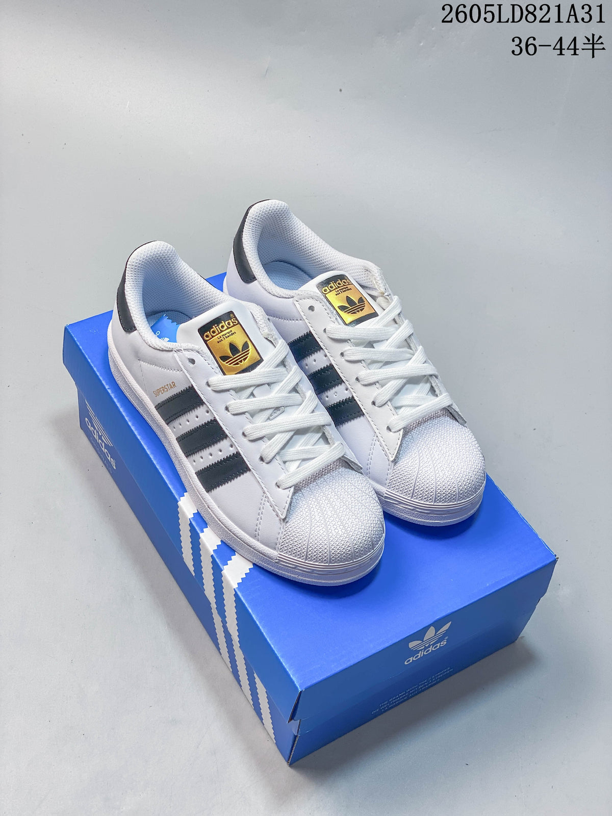 Pair of white Adidas Superstar sneakers with dark stripes and shell toes, displayed on a blue shoe box.