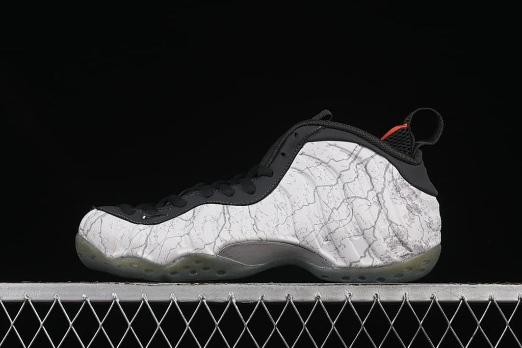 Side view of white and gray patterned Nike Air Foamposite One sneakers with black trim and orange accents.