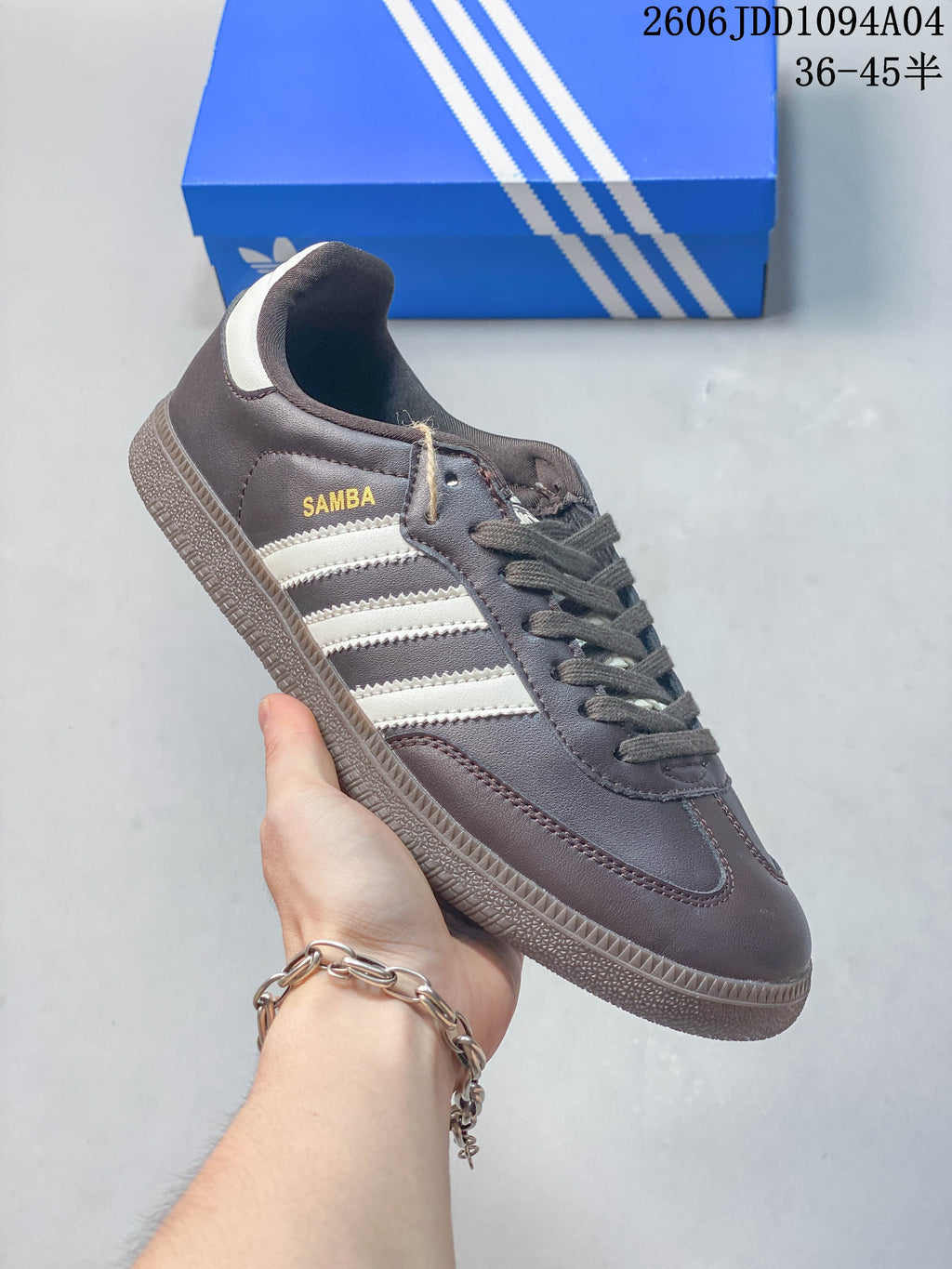 Side view of a brown-grey Adidas Samba sneaker with light stripes, gold Samba lettering, and a textured sole.