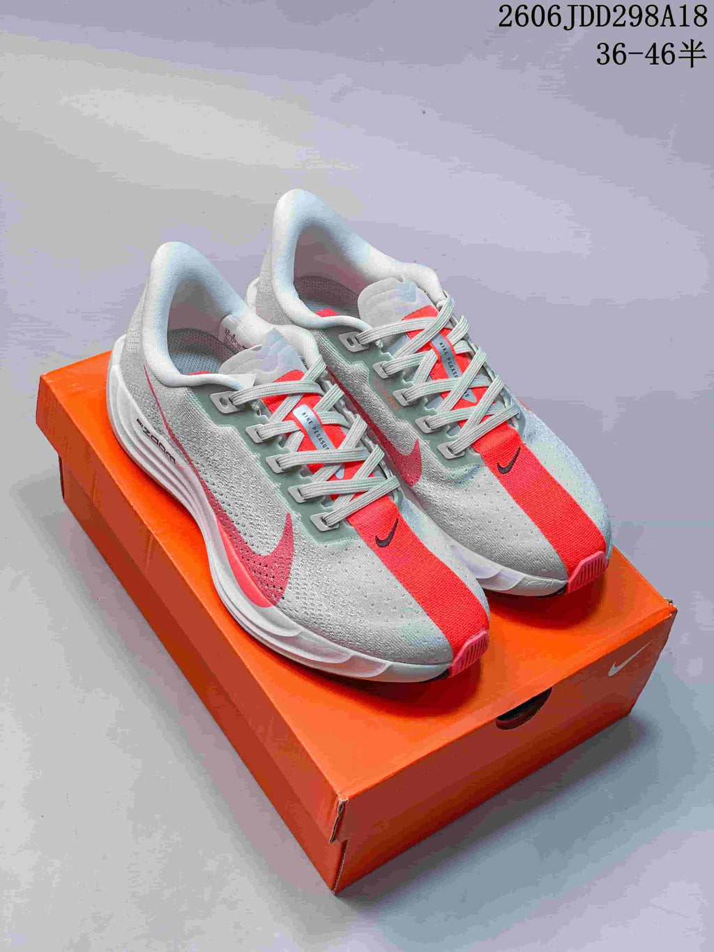 Pair of gray and coral Nike Pegasus running shoes displayed on an orange shoe box