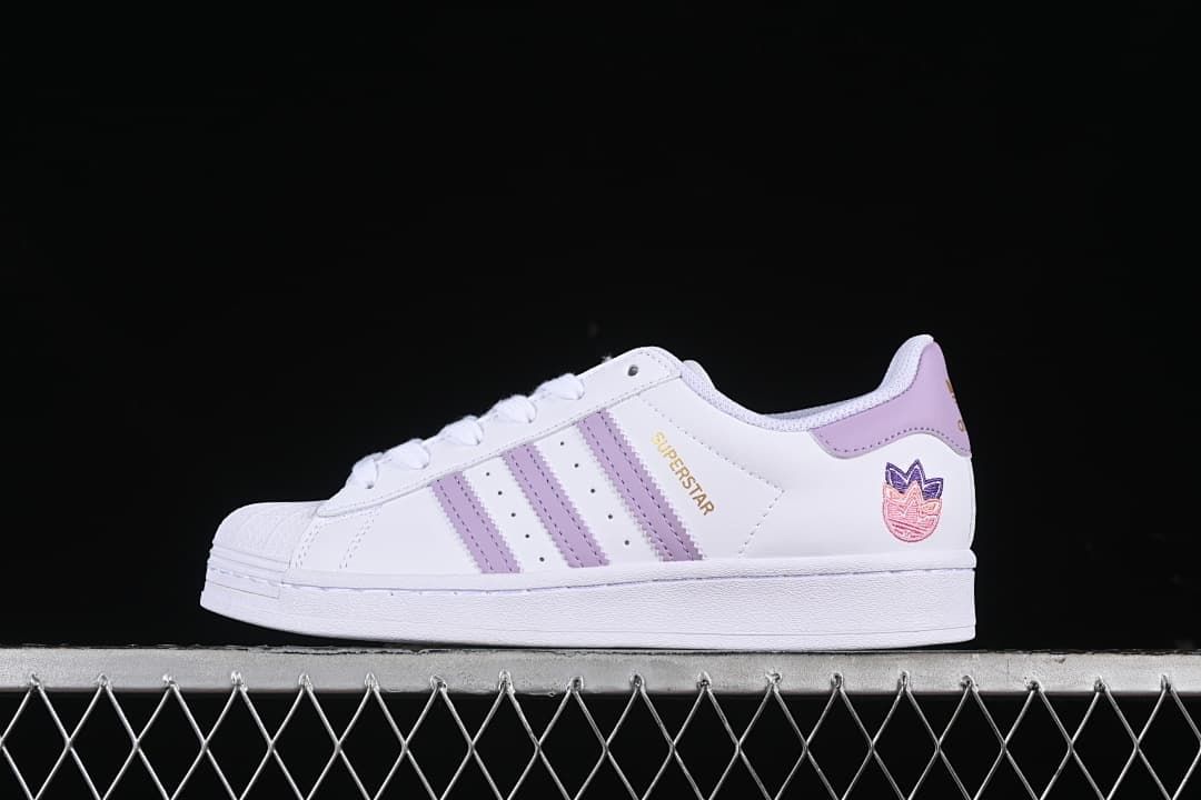 Side view of a white adidas Superstar sneaker with lavender stripes and heel accents