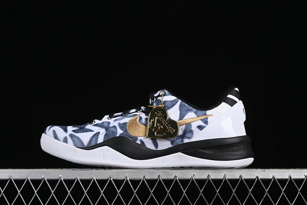 Side view of a Nike Kobe 8 Protro shoe with a white and navy patterned upper, gold swoosh, black midsole accents, and heart-shaped charm.