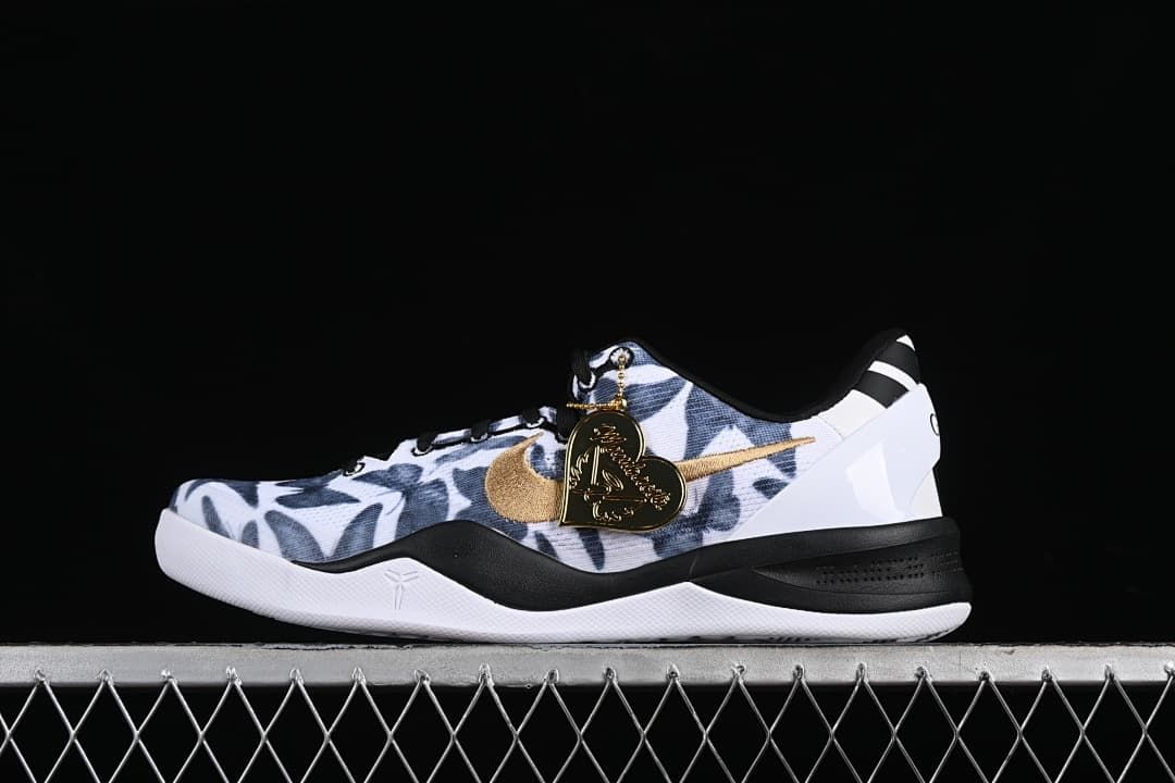 Side view of a Nike Kobe 8 Protro shoe with a white and navy patterned upper, gold swoosh, black midsole accents, and heart-shaped charm.