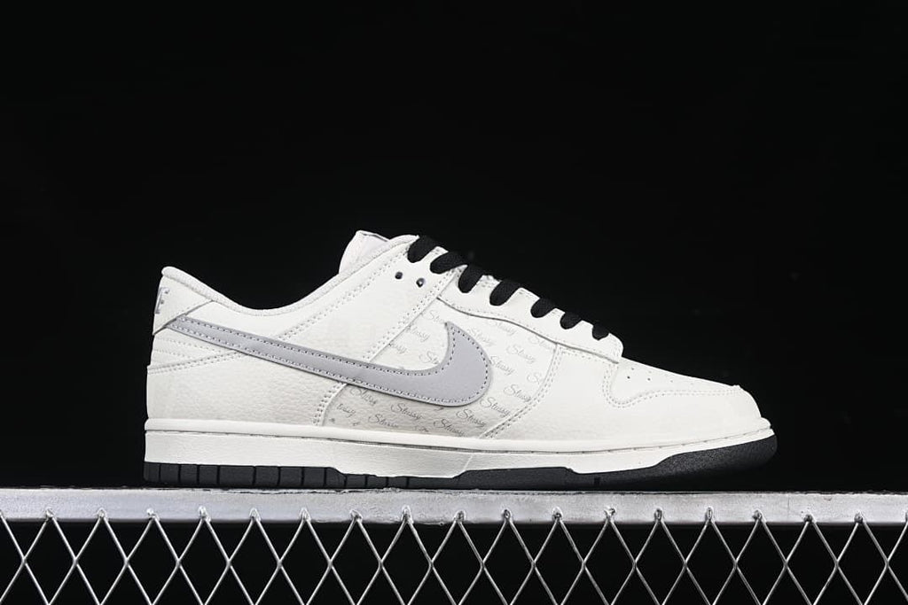 Side profile showing the white upper, grey Swoosh, Stüssy script and black outsole.