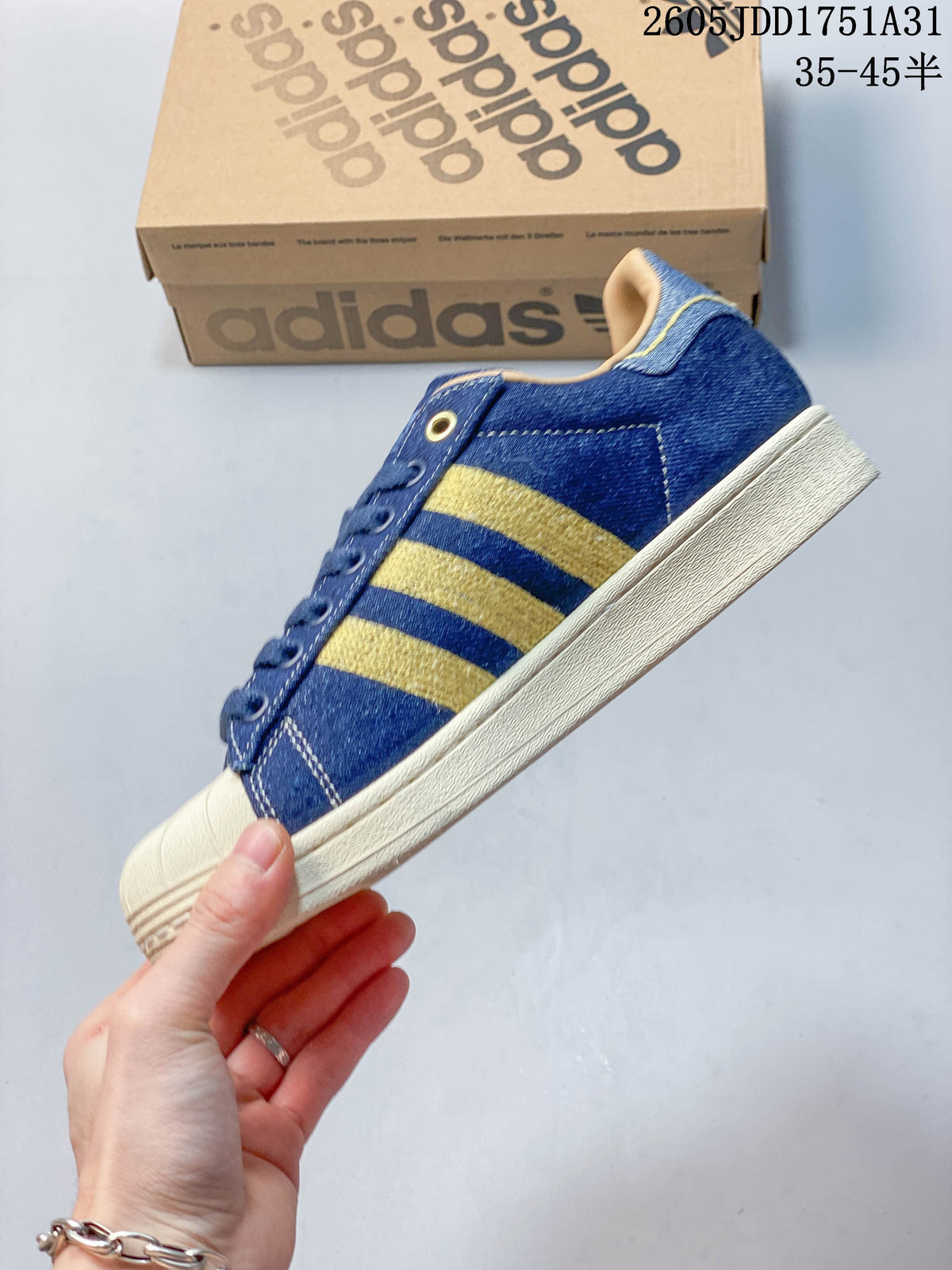Side view of a blue denim-look Adidas Superstar sneaker with gold-tone stripes and a cream sole