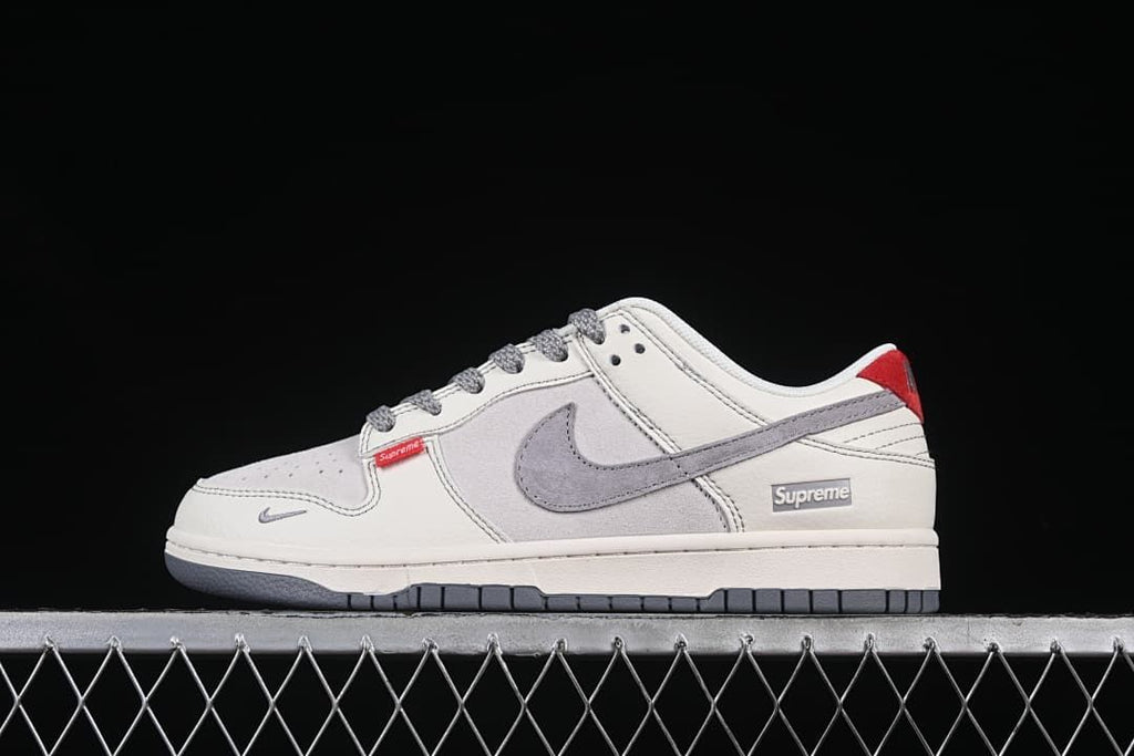 Side view of an off-white and grey Nike SB Dunk Low sneaker with red heel accent and grey swoosh.