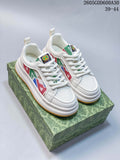 Pair of white Gucci Screener GG-style sneakers with multicolor geometric side panels and gum-colored outsoles, shown on a patterned box.