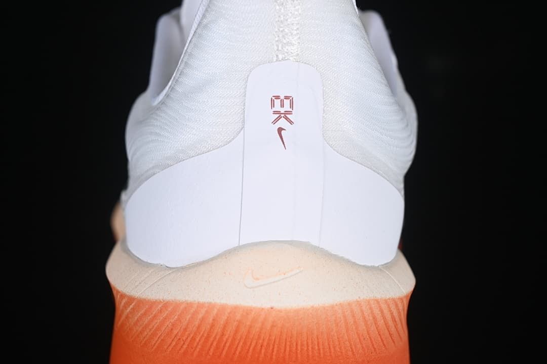 Rear view of the white shoe with coral-orange midsole