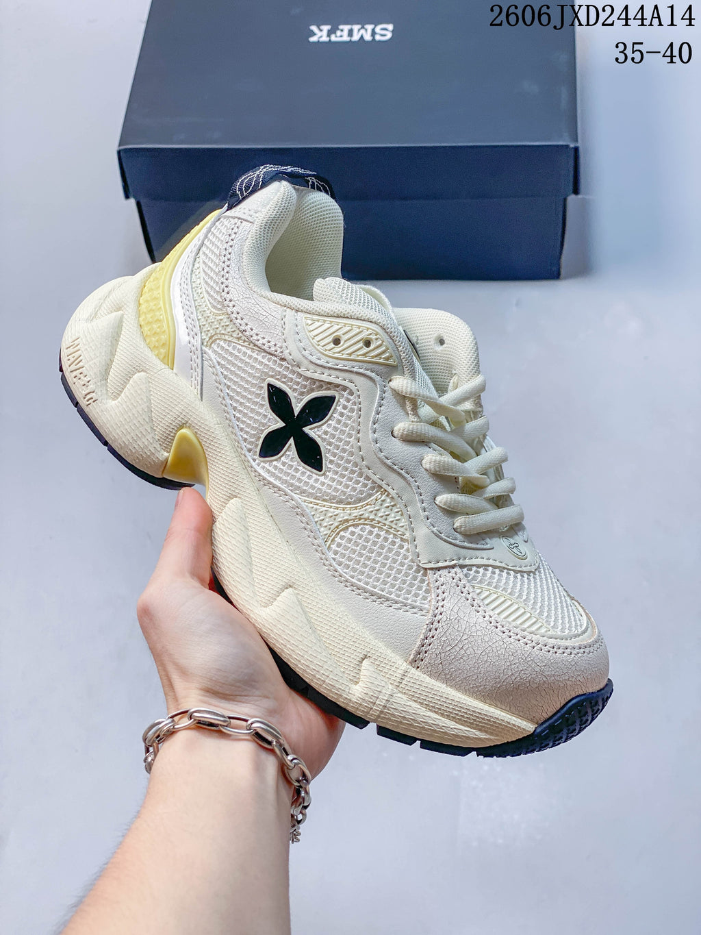Side view of the sneaker with a black emblem, ivory-toned panels, pale yellow accents, and a chunky sole.