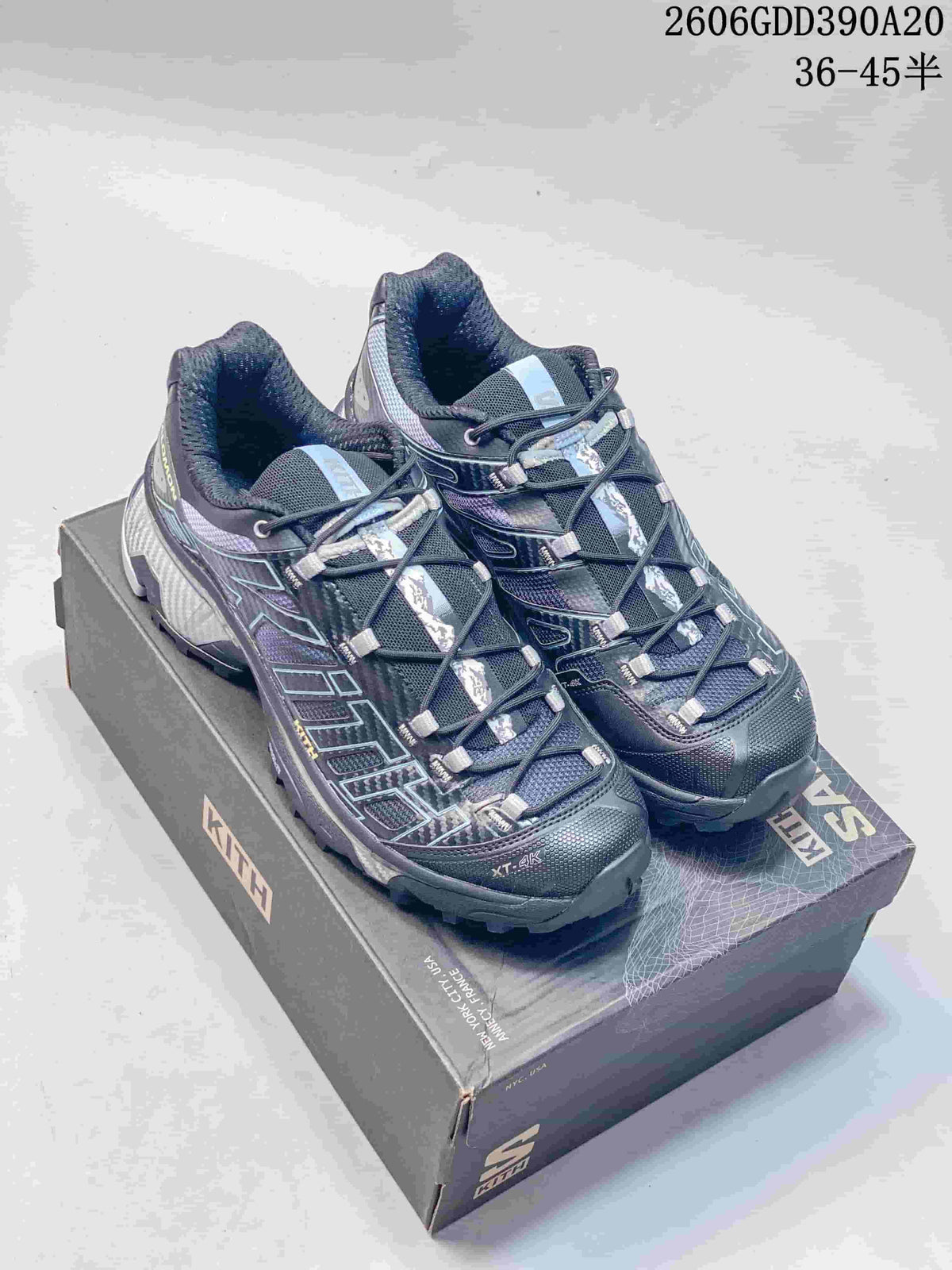 Pair of dark blue-gray Salomon XT-4K shoes with patterned details and quick-lacing, displayed on a Kith box.