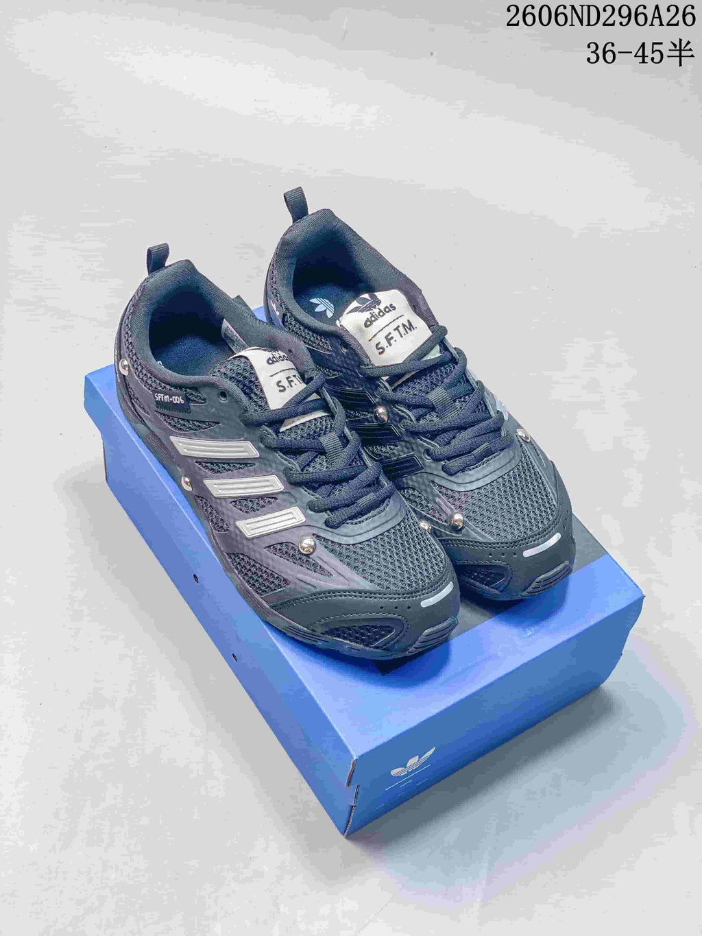 Pair of dark gray Adidas SFTM-006 low-top sneakers shown from above on a blue box