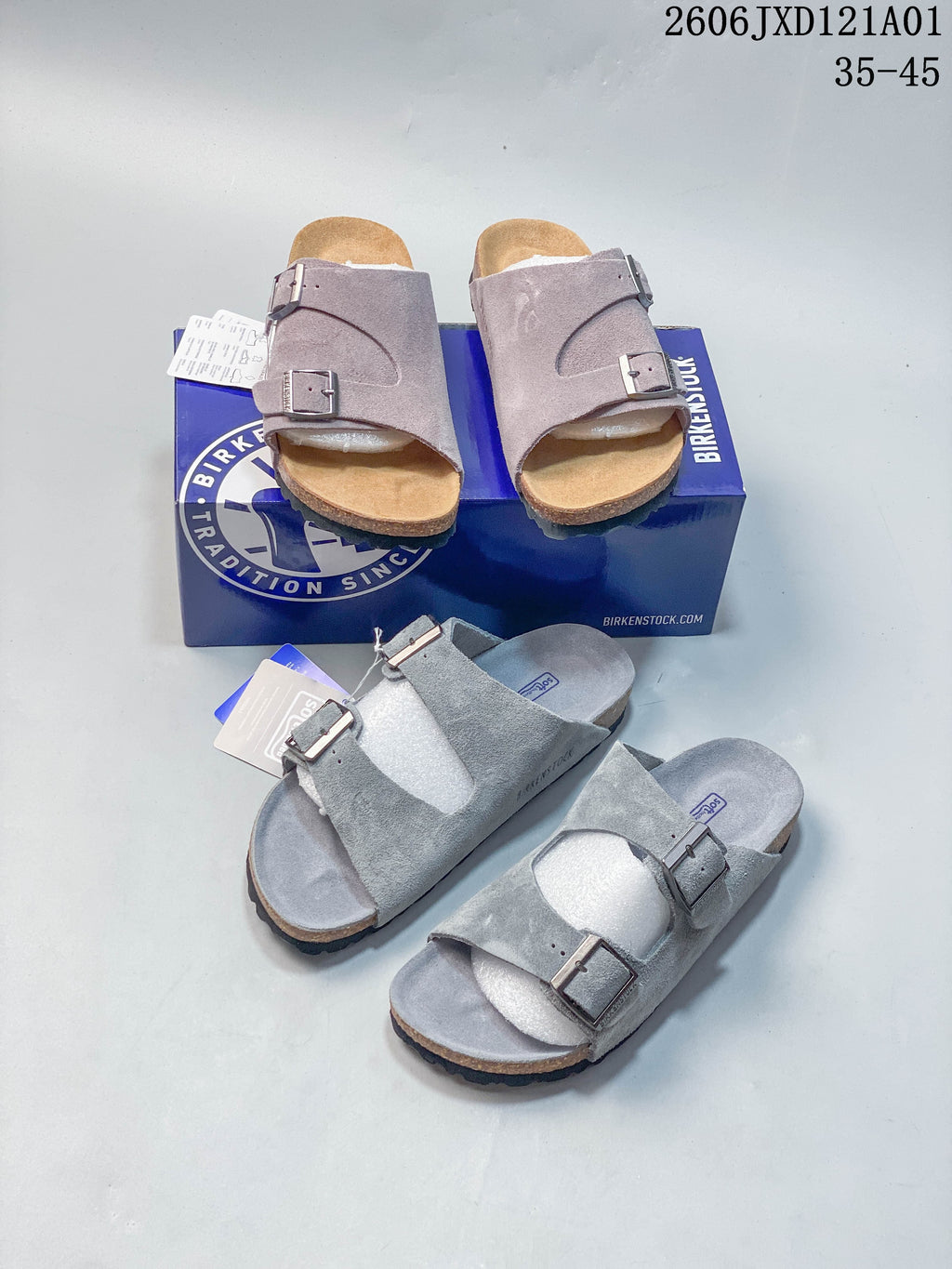 Muted mauve and gray two-strap sandals shown together with a blue shoe box.