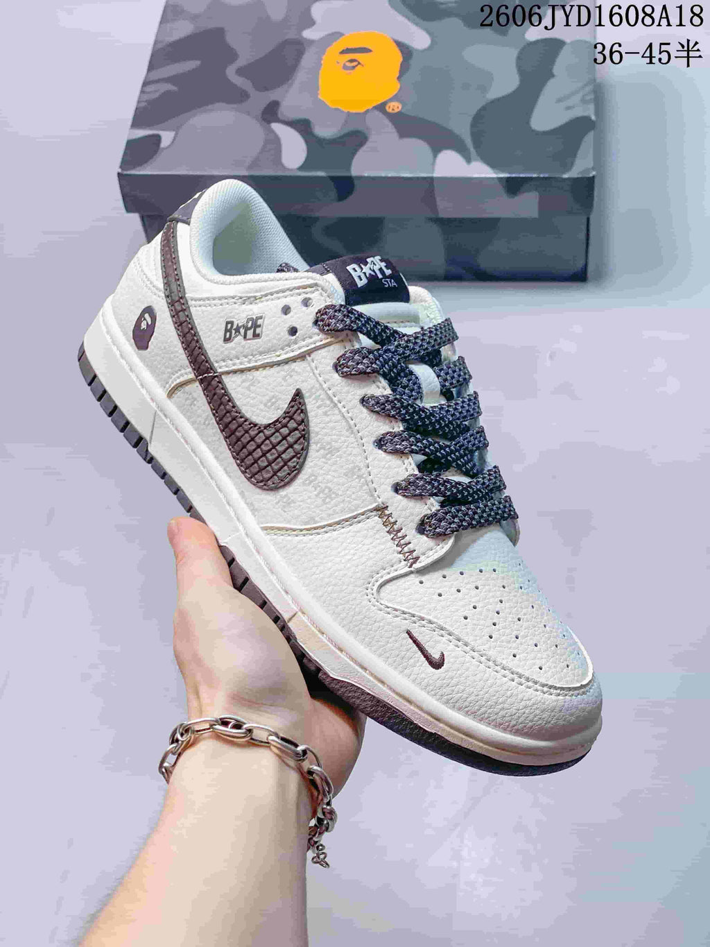 Angled view of a cream sneaker with dark accents, patterned laces, and a camouflage-patterned box