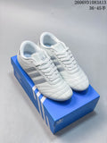 Pair of white adidas Originals Taekwondo lace-up sneakers with silver-tone stripes on a blue box.