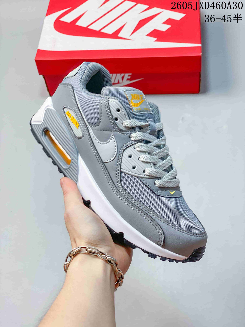 Angled side view of the grey Nike Air Max 90 sneaker with white and yellow accents.