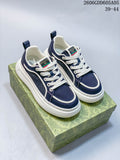 Navy Gucci-branded lace-up sneakers with white piping and thick white soles, photographed on a patterned box.