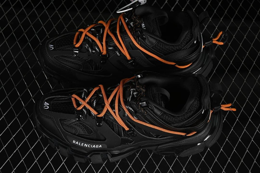 Pair of black Track sneakers with orange laces, viewed from above.