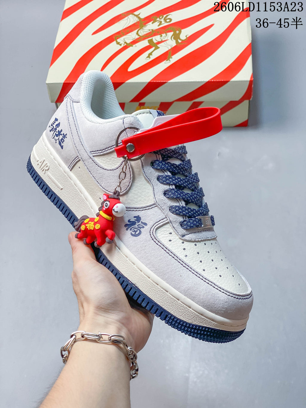 Close view of a pale gray and white low-top sneaker with navy outsole and a red hanging charm
