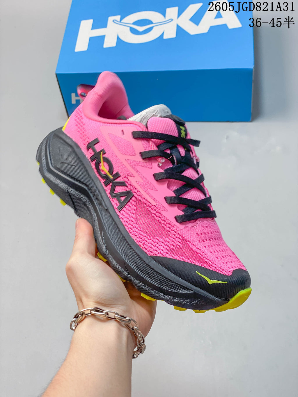 Angled side view of the pink shoe with HOKA branding, dark midsole and yellow tread accents.