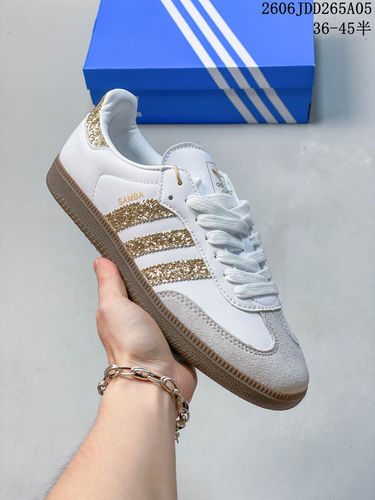 Side view of a white adidas Samba OG sneaker with gold glitter stripes, pale gray overlays, and a gum-colored outsole.