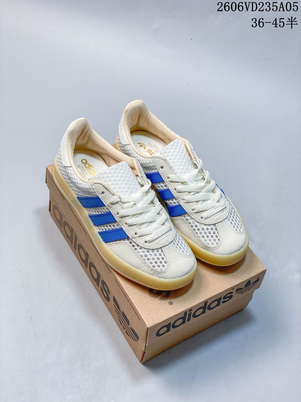 White and light grey adidas Samba sneakers with blue stripes and gum-look soles, shown on a shoebox