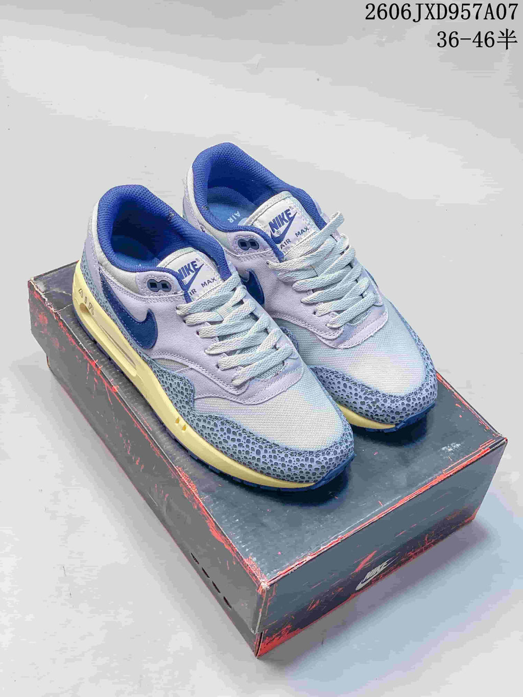 Pair of Nike Air Max 1 '86 Premium sneakers in gray-lavender, blue, and cream, shown on a shoe box.