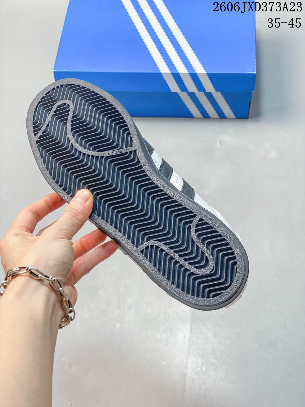 View of the dark patterned outsole on a white and dark gray Superstar sneaker.