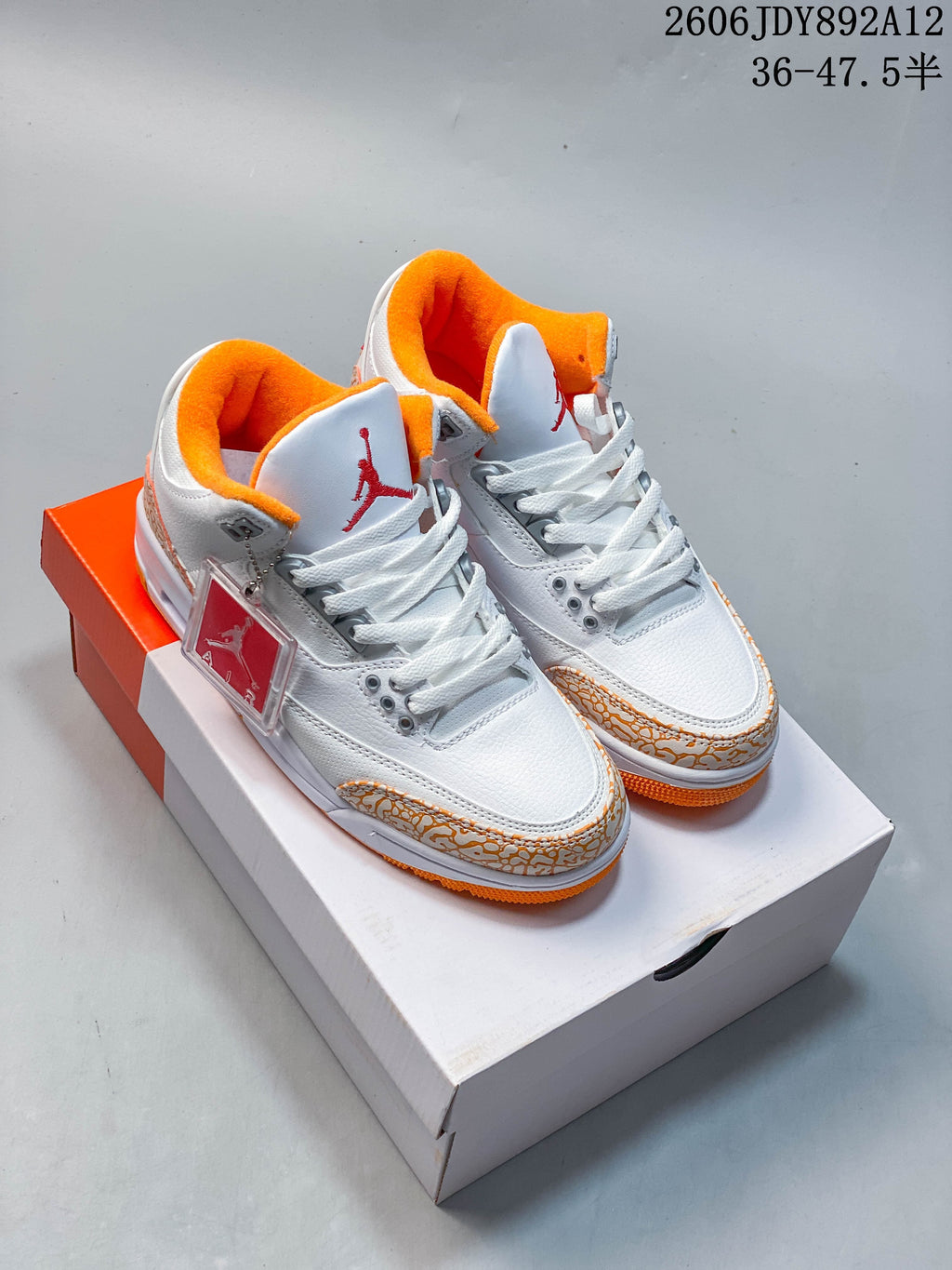 Pair of white and orange Air Jordan 3 Retro sneakers displayed on a shoebox.