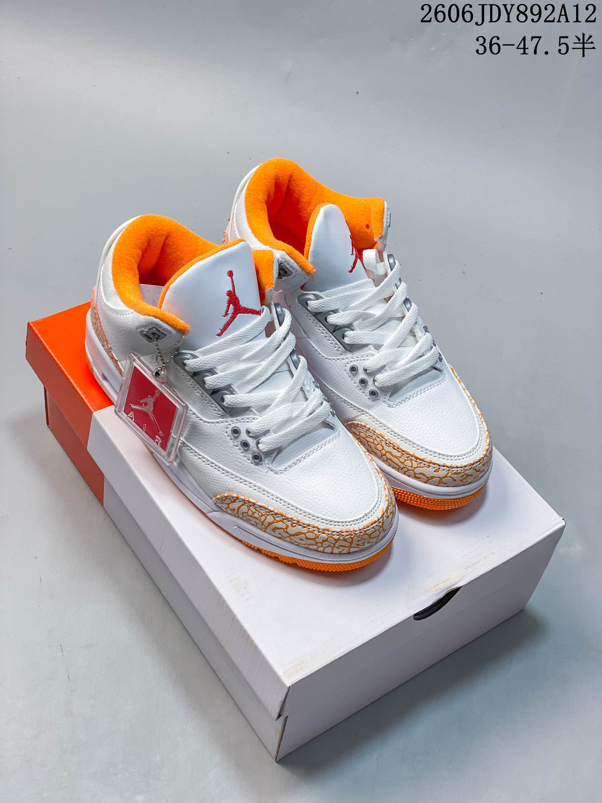 Pair of white and orange Air Jordan 3 Retro sneakers displayed on a shoebox.