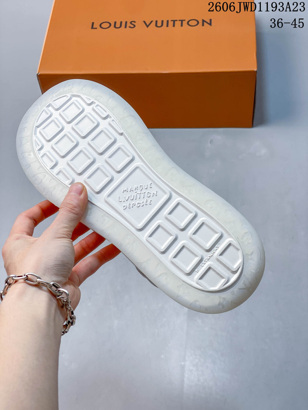 Underside of a white sneaker showing geometric tread and orange shoe box
