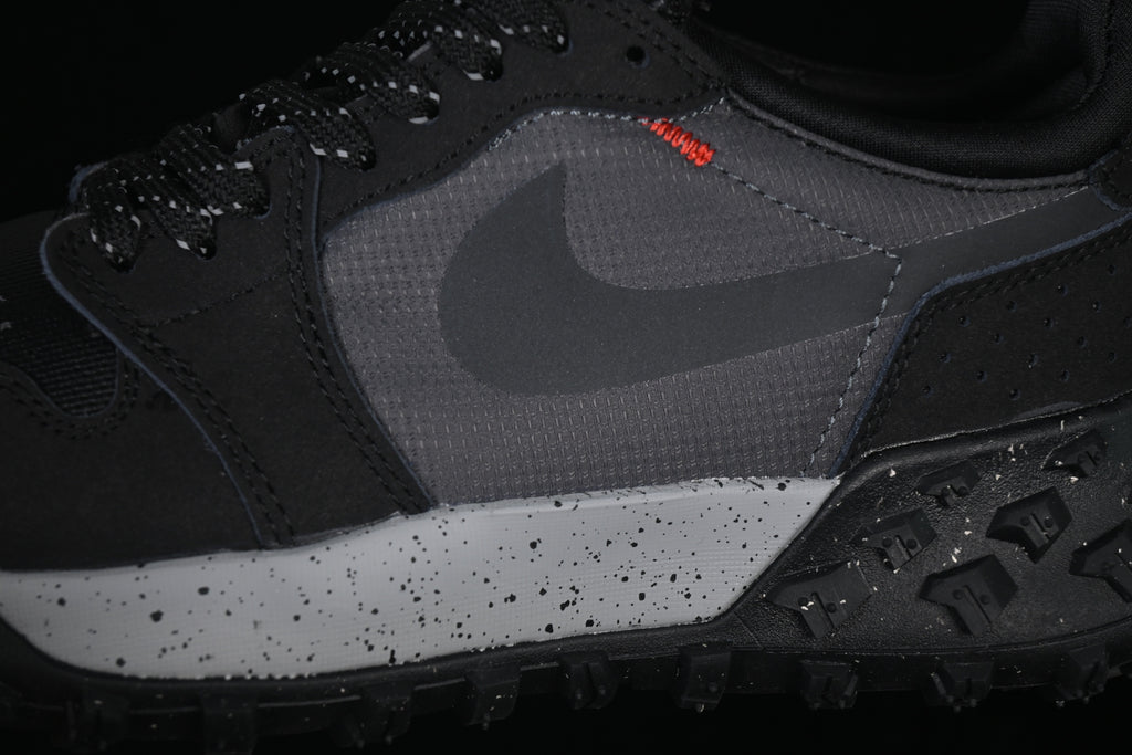 Close-up of the dark gray side panel, black Swoosh, orange stitching, and speckled midsole